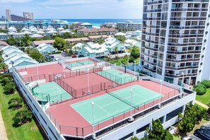 Un immeuble à plusieurs étages, doté d’un court de tennis sur le toit, entouré d’immeubles résidentiels et offrant une vue sur l’océan.