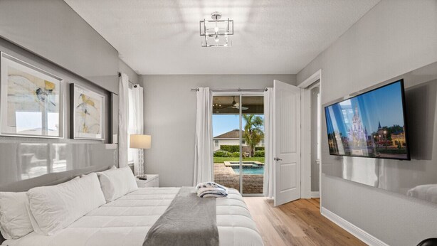 A modern bedroom with a large bed, a TV on the wall, and a view of a swimming pool and house outside.