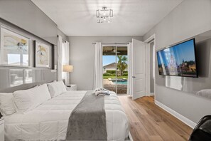 A modern bedroom with a large bed, a TV on the wall, and a view of a swimming pool and house outside. - 8 Bedroom 6.5 Bathroom Encore at Reunion 7644 (Kissimmee)