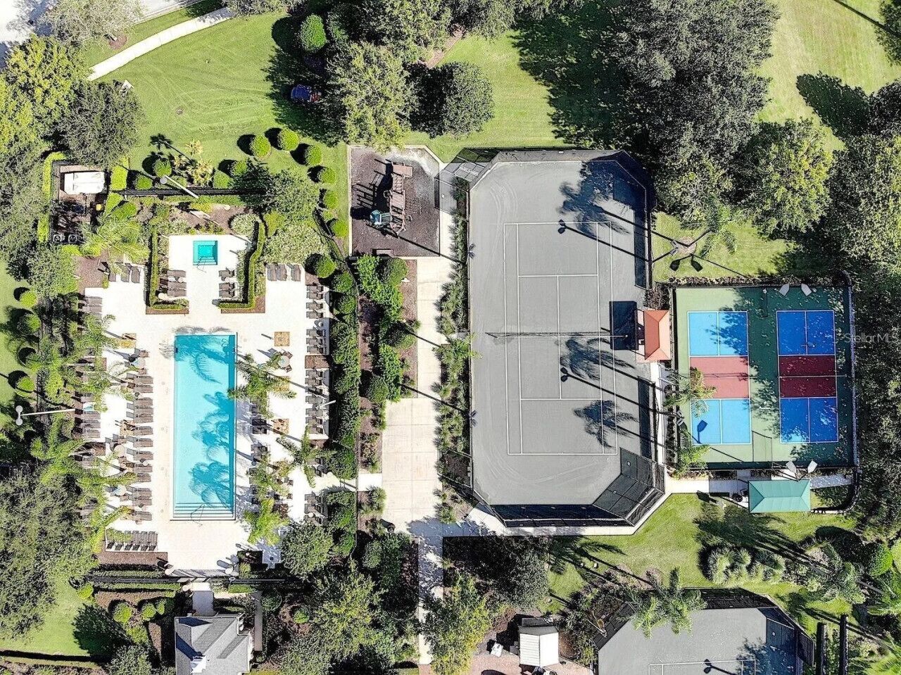 An aerial view of a resort with a swimming pool, tennis courts, and landscaped areas.