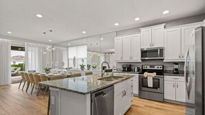 A modern kitchen with white cabinets, stainless steel appliances, and a granite countertop island.