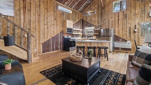 A rustic cabin interior with a kitchen, dining area, and seating space.