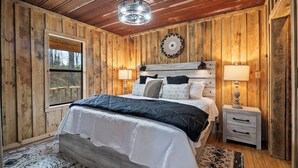 A wooden-paneled bedroom with a large bed, two bedside tables, a hanging light fixture, and a window.