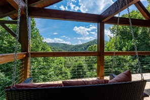 A wooden deck with a swing chair overlooking a forested mountain landscape.