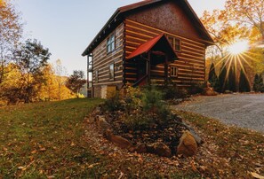 A log cabin with a porch, surrounded by a grassy area with a