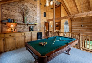 A wooden interior with a pool table, a coffee machine, and a rustic decor including a fur rug.