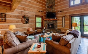 A log cabin interior with a stone fireplace, leather sofas, and a wooden coffee table.