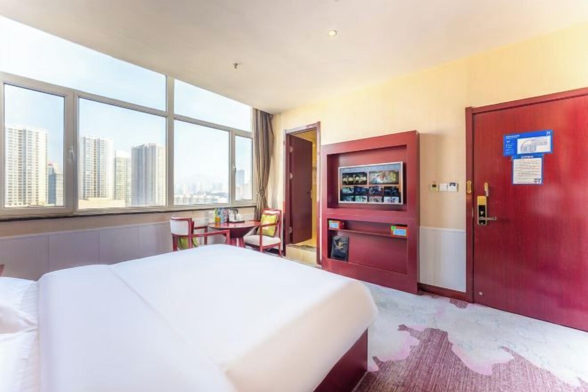 Une chambre d’hôtel avec un grand lit, une télévision, un bureau et une vue sur le paysage urbain par la fenêtre.