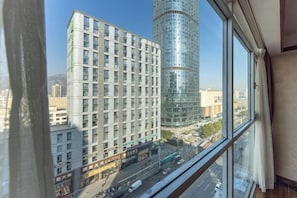 A view from a window overlooking a cityscape with modern buildings, a clear sky, and a street with vehicles.