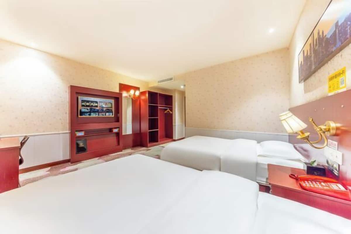 A hotel room with two beds, a wardrobe, a desk with a telephone, and a wall-mounted TV.