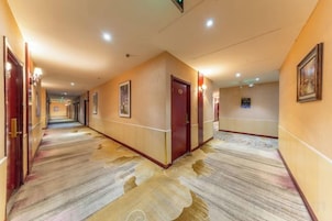 A hotel corridor with carpeted floors, doors, and wall-mounted lighting.