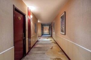 Un pasillo de hotel con puertas, cuadros enmarcados y una alfombra estampada.
