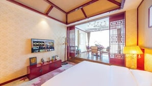 A hotel room with a large bed, a red cabinet with various items, a television mounted on the wall, and a view of the outside through a sliding door.