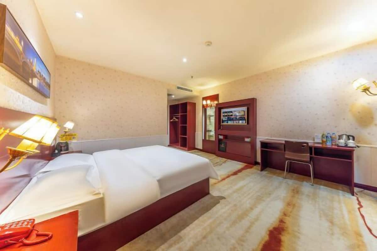 A hotel room with a bed, desk, chair, and a TV on a stand.