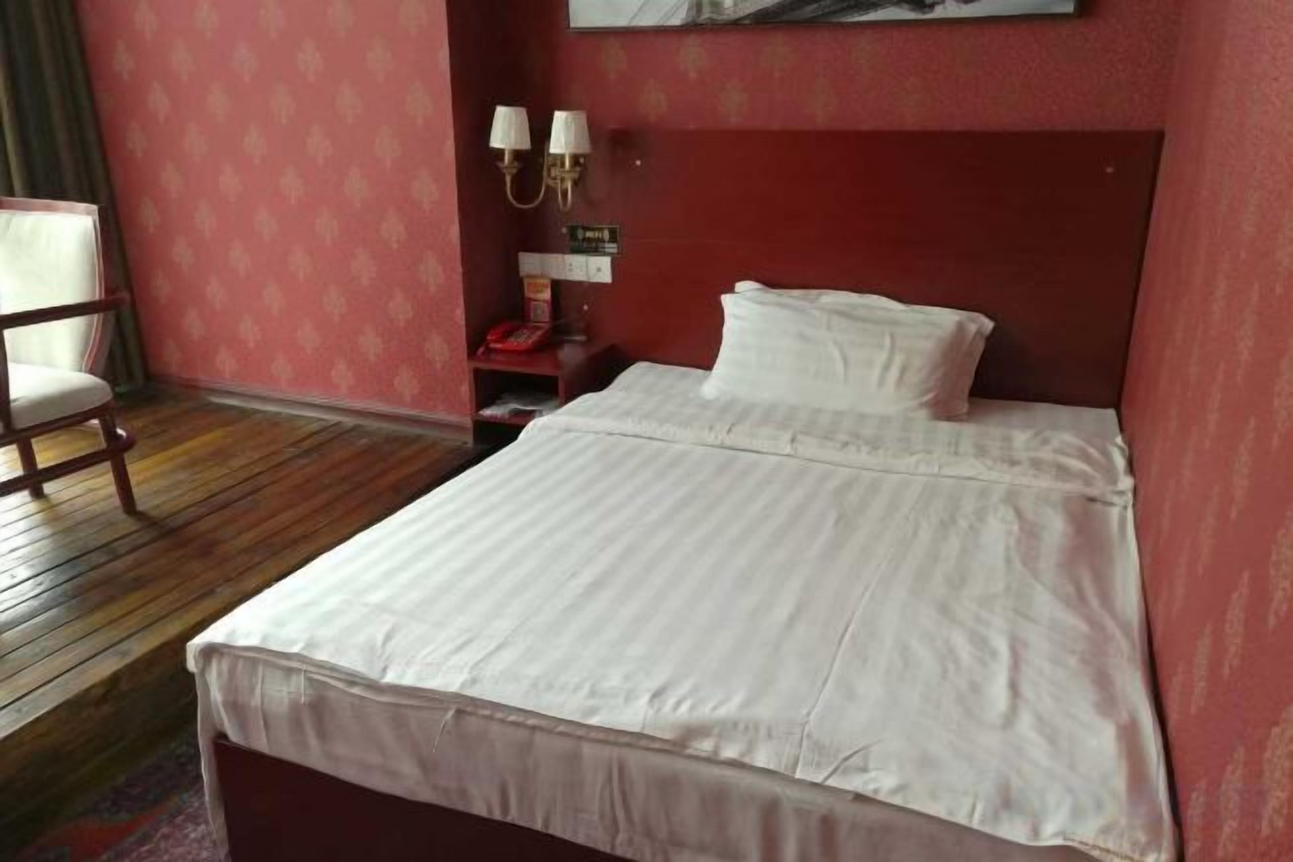 A bed with white linens in a room with a red wall and a wooden floor.