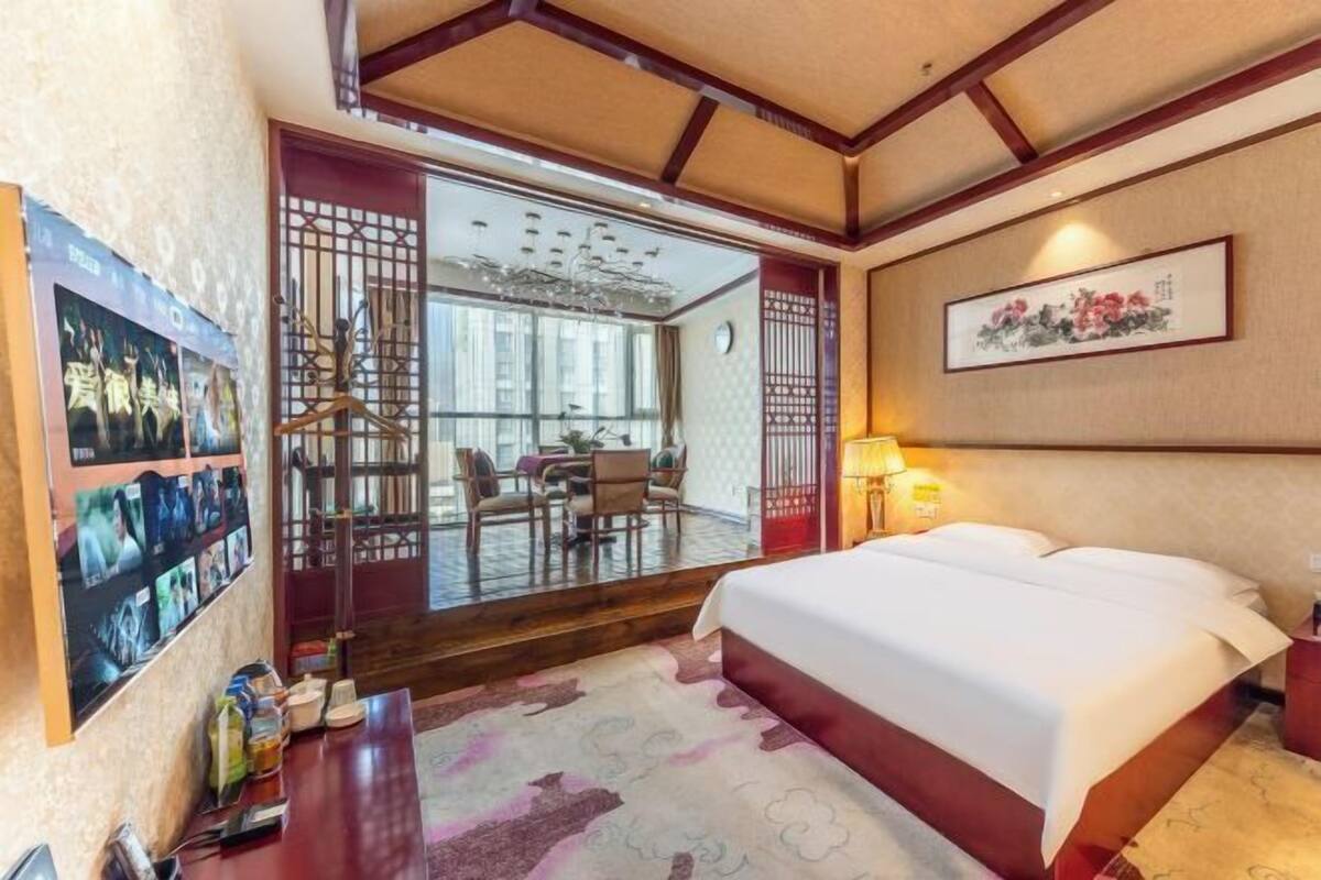A hotel room with a bed, a desk, a chair, a table, and a view of the outside.