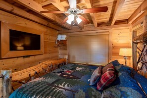 A wooden cabin room with a bed, a ceiling fan, a mounted TV, and a window with blinds. - Hawk's Landing-Private Luxury Log Cabin Rental, Mountain Views, High Speed Internet, Hot Tub - 15 minutes from the NOC! (Topton)