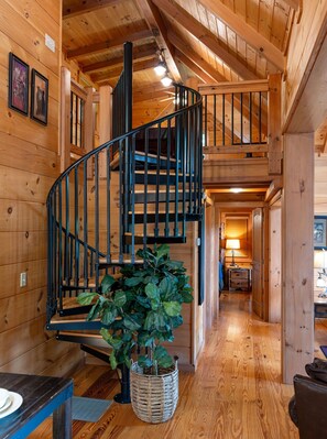 A wooden interior with a spiral staircase, a dining area, and a hallway leading to a bedroom. - Hawk's Landing-Private Luxury Log Cabin Rental, Mountain Views, High Speed Internet, Hot Tub - 15 minutes from the NOC! (Topton)
