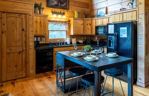 Ein Holzblockhaus-Interieur mit einer Küche, die einen schwarzen Kühlschrank, Holzschränke und eine Essecke mit Hockern zeigt.
