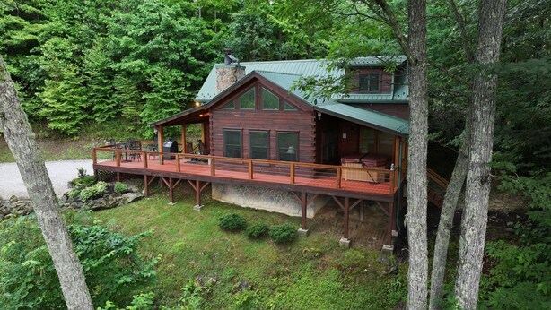 A cabin with a deck, a stone foundation, and a green roof, surrounded by trees. - Hawk's Landing-Private Luxury Log Cabin Rental, Mountain Views, High Speed Internet, Hot Tub - 15 minutes from the NOC! (Topton)
