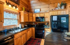 A kitchen with wooden cabinets, a black refrigerator, a microwave, and a stove. - Hawk's Landing-Private Luxury Log Cabin Rental, Mountain Views, High Speed Internet, Hot Tub - 15 minutes from the NOC! (Topton)
