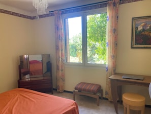 A bedroom with a bed, a desk, a chair, a mirror, and a window with curtains.