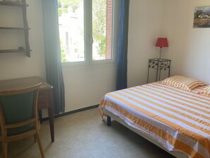 Et værelse med seng, skrivebord, stol, lampe og et vindue.