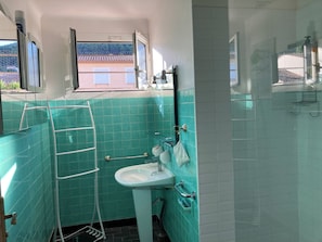 A bathroom with teal tiles, a white sink, a mirror, and a window with a view of buildings.