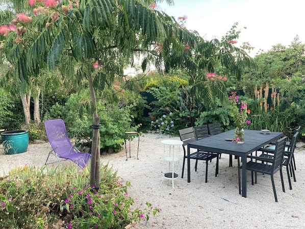 An outdoor seating area with a table and chairs, surrounded by various plants and trees.