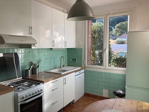 A kitchen with a gas stove, sink, and window with a view of greenery.