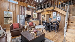 A rustic cabin interior with a dining area, kitchen, and seating space.