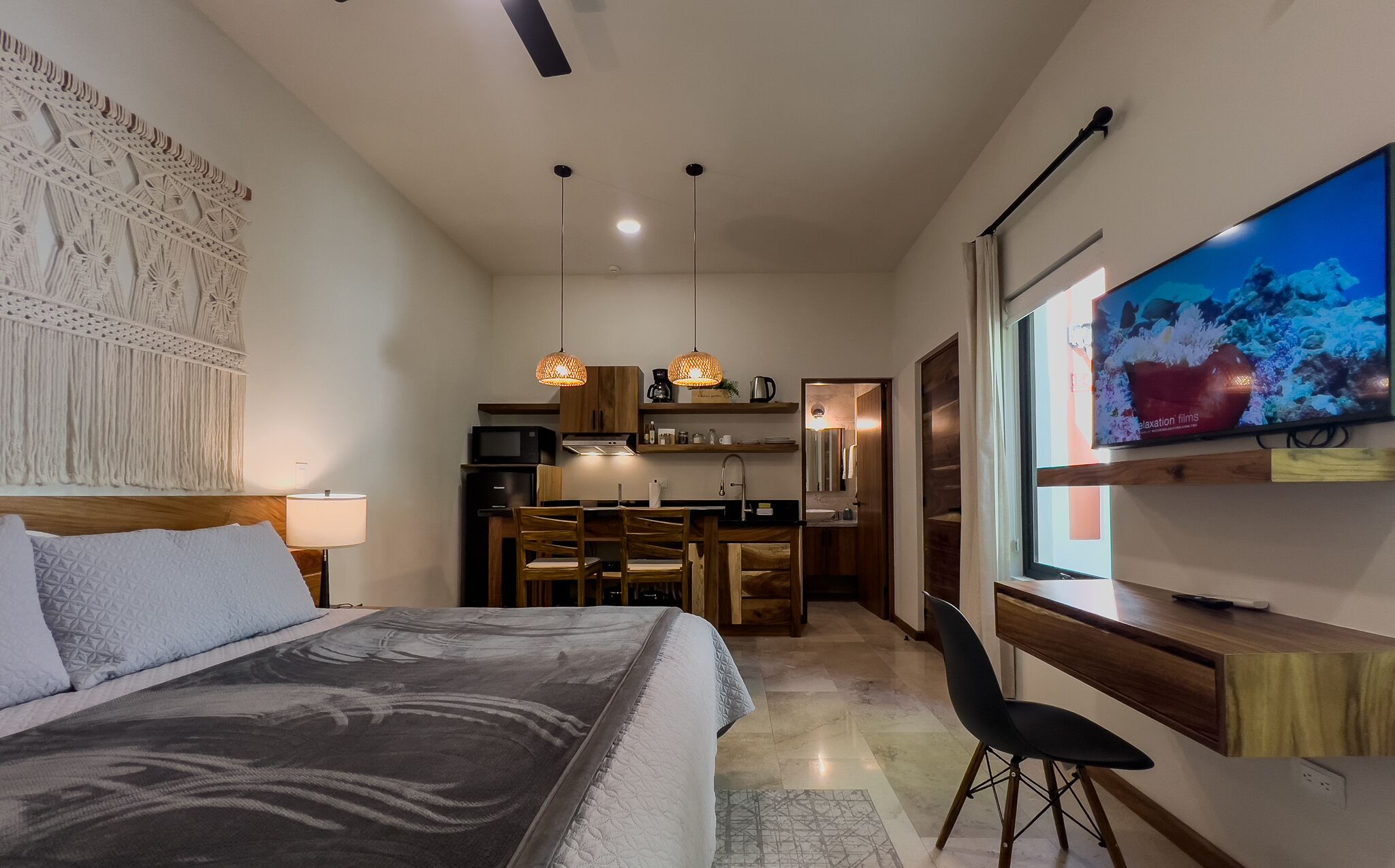 Een moderne hotelkamer met een bed, een bureau, een televisie en een kitchenette.