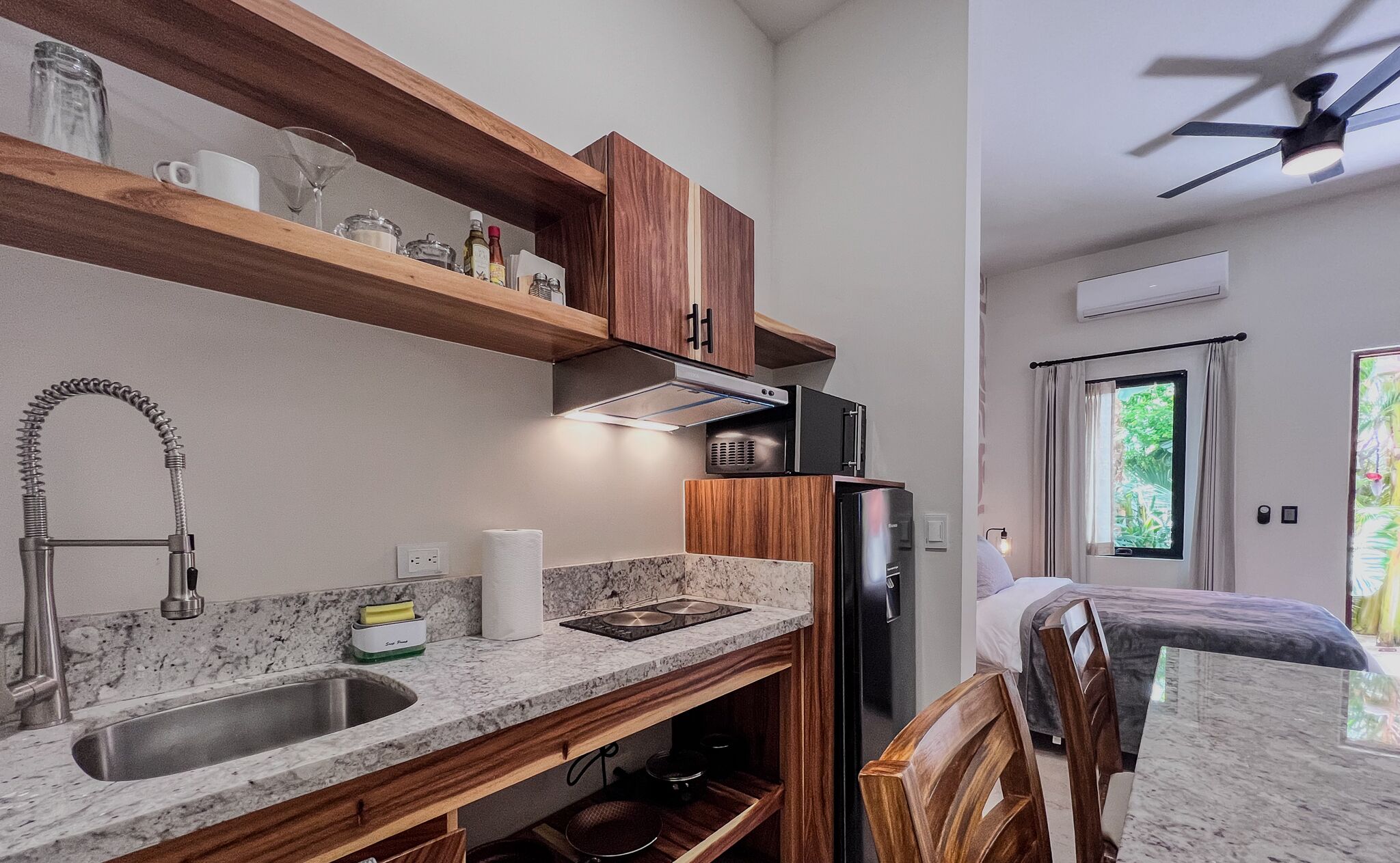 Una cocina compacta con un lavamanos empotrado, repisas de madera, un refrigerador y un ventilador de techo.