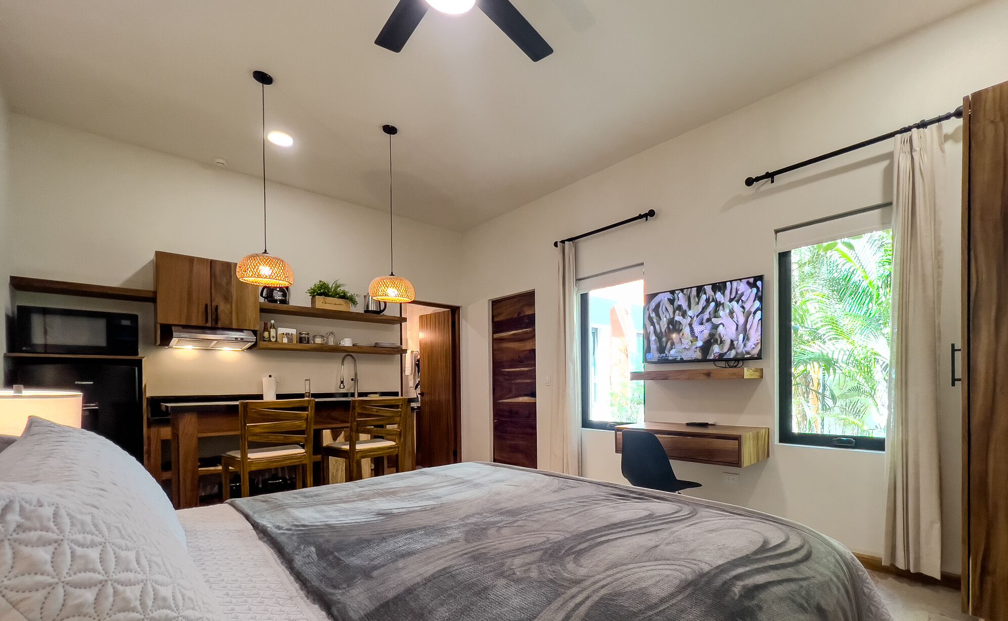 Un dormitorio moderno con una cama grande, un escritorio, un televisor y una kitchenette.