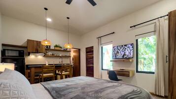 Un dormitorio moderno con una cama grande, un escritorio, un televisor y una kitchenette.