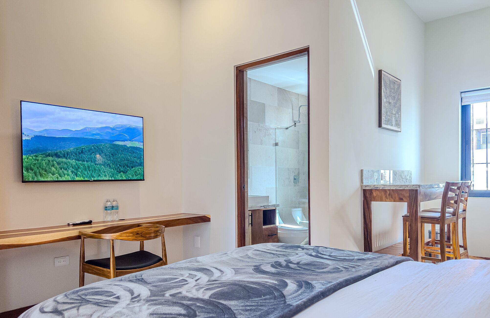 A bedroom with a bed, a desk, a chair, a TV, and a shower.