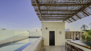 Un área de piscina en la azotea con un espacio de estar techado y una puerta que da a un ambiente interior.