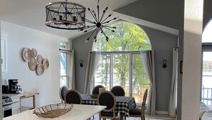 Een moderne keuken met een centraal eiland, een eethoek met geruit tafelkleed en een groot raam met gordijnen.