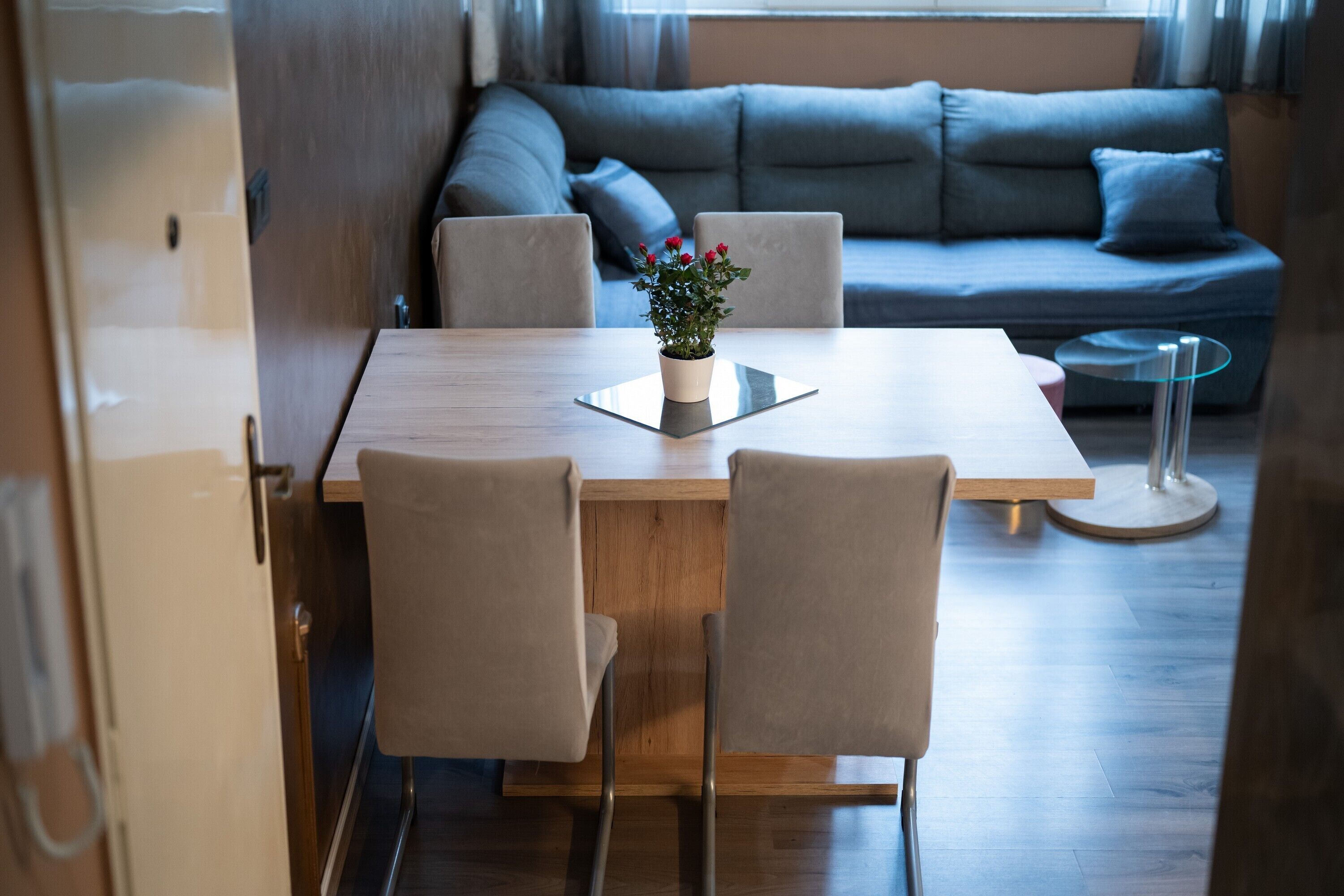 Un salon moderne avec une table à manger en bois, quatre chaises, un canapé gris et une petite plante en pot.