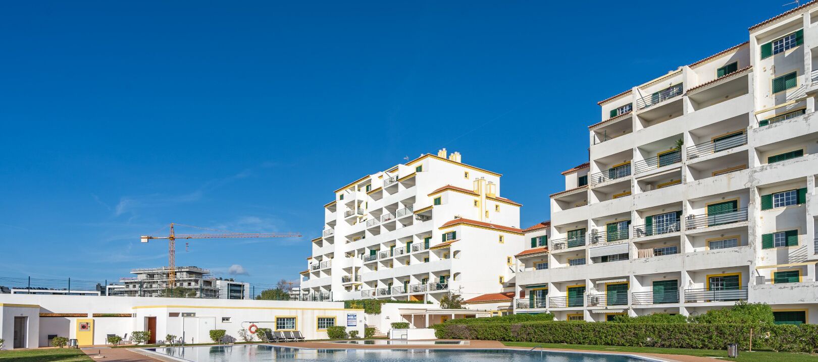 Un complesso residenziale moderno con numerosi balconi, una piscina e una gru edile sullo sfondo.