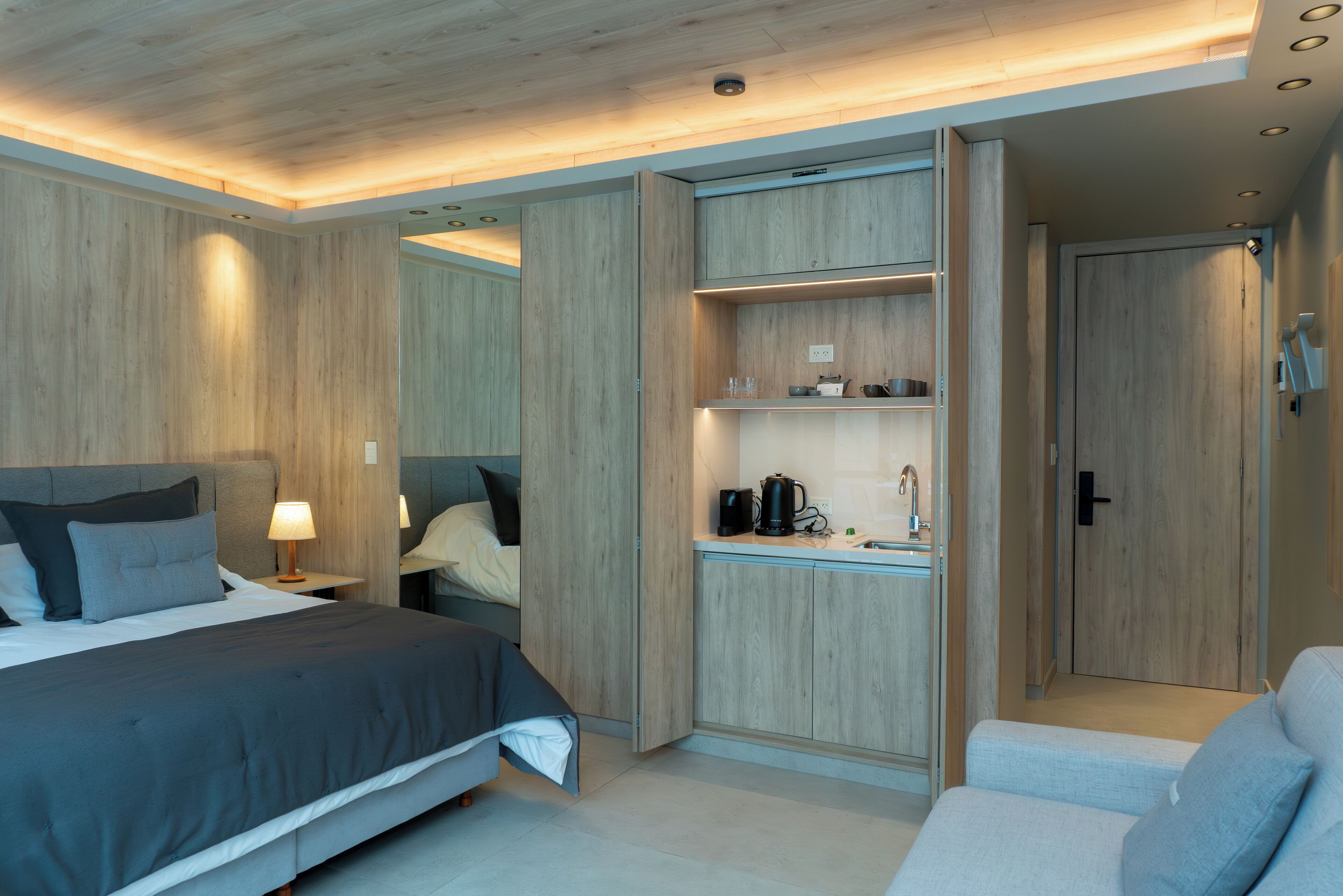 Ein modernes Hotelzimmer mit Bett, Nachttisch, Lampe und integriertem Stauraum.