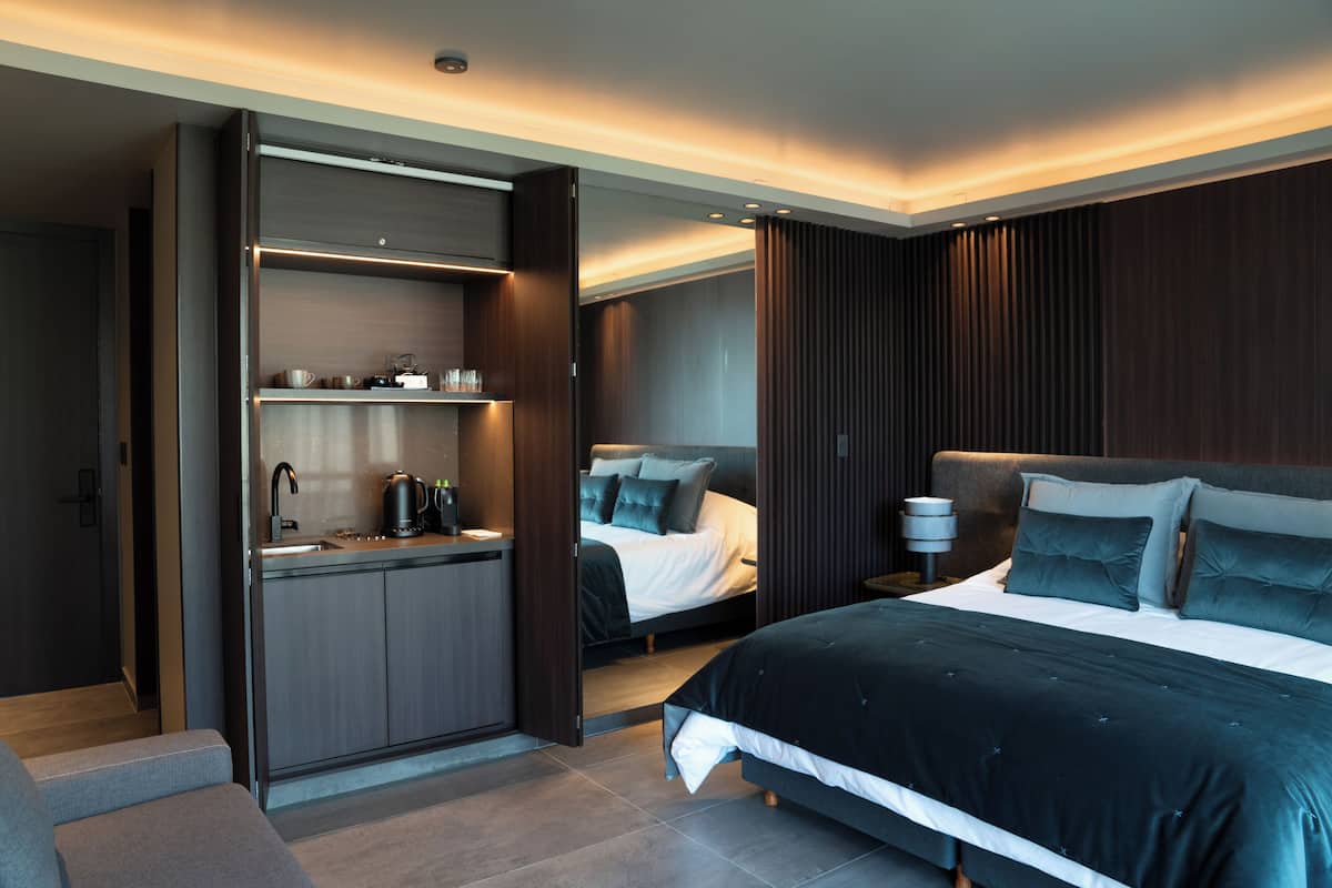 A modern hotel room with a built-in kitchen, a large bed, and a separate sleeping area.