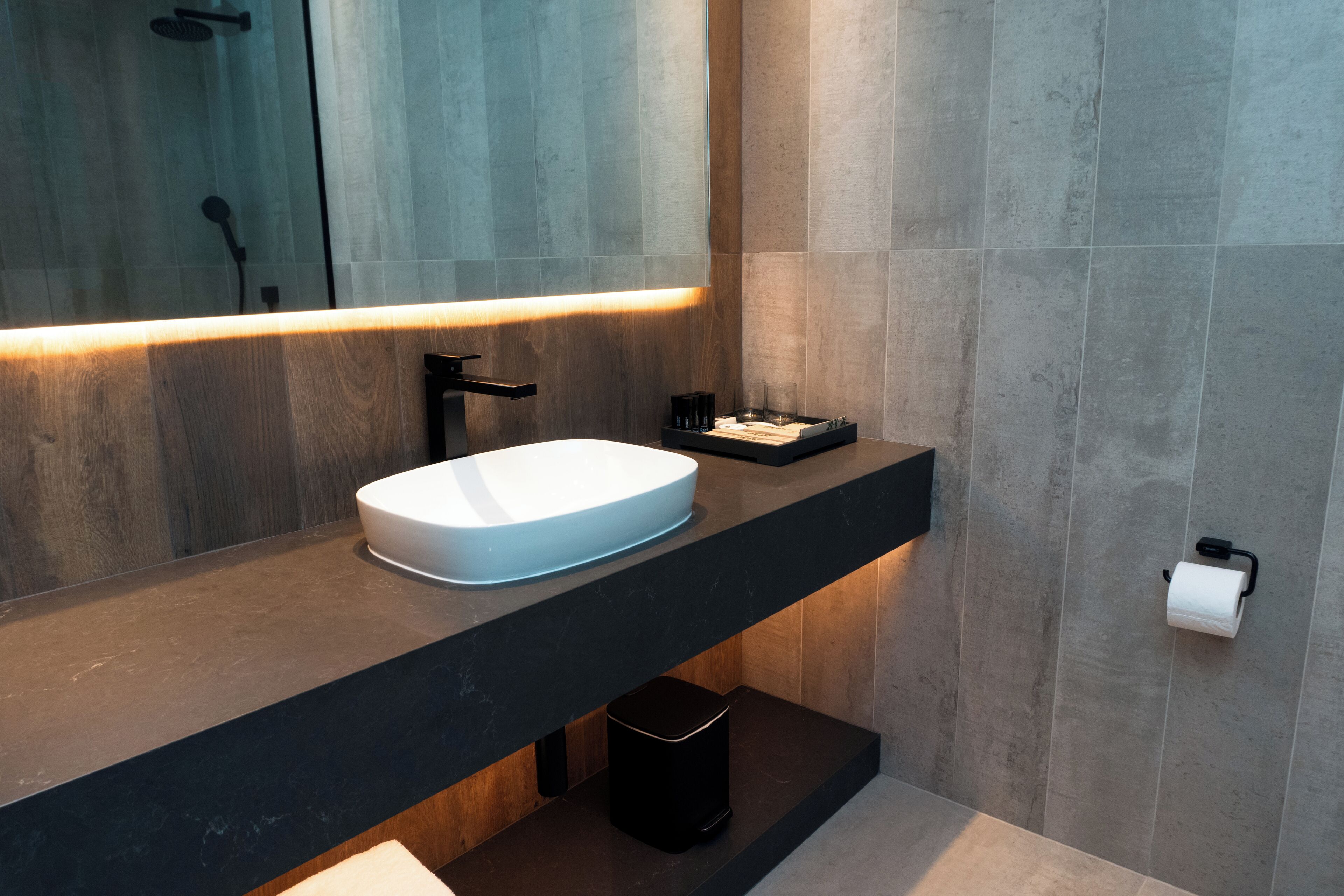 A modern bathroom with a large mirror, a white sink, a black faucet, and a towel rack.