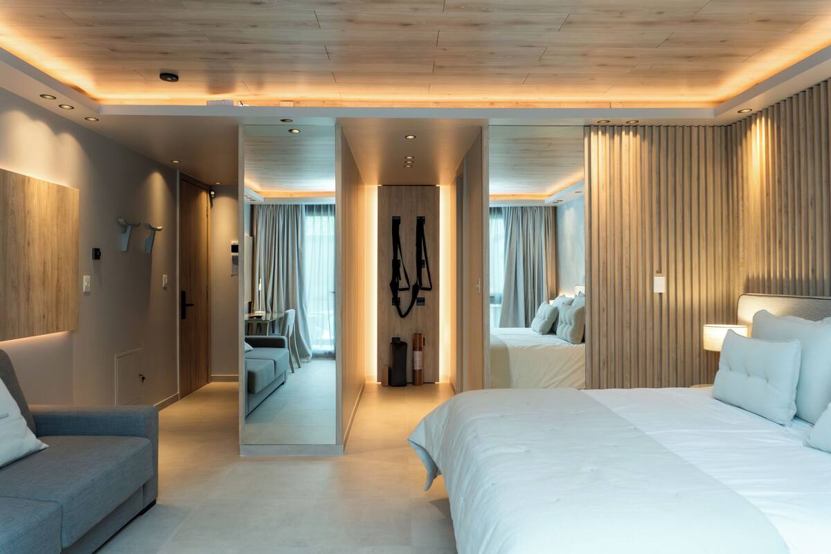 A modern hotel room with a large bed, a sofa, a mirror, and a wooden panel wall.