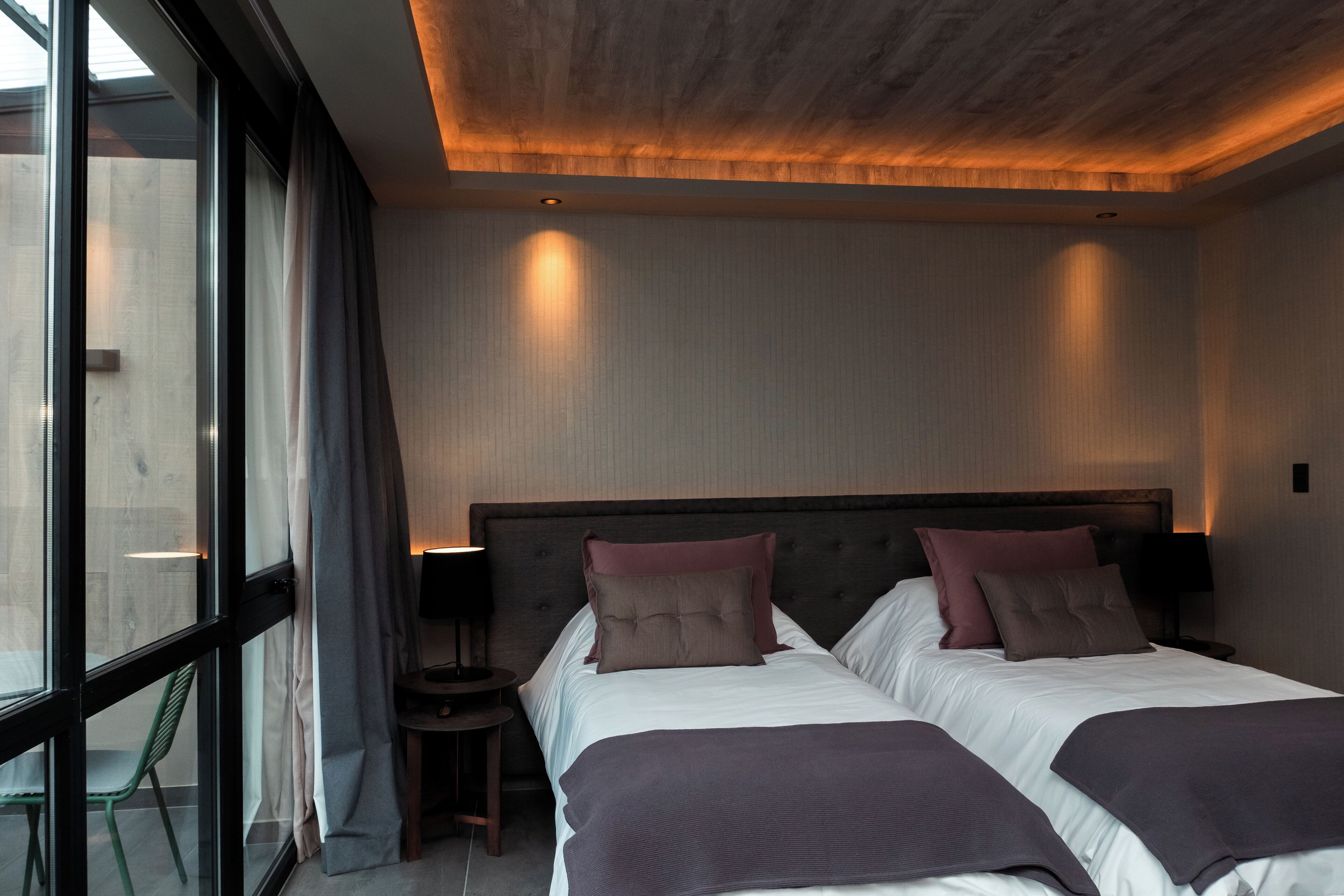A modern hotel room with two beds, a large window, and a view of the outside.