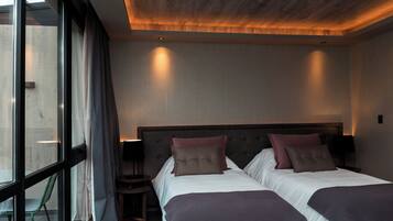 A modern hotel room with two beds, a large window, and a view of the outside.