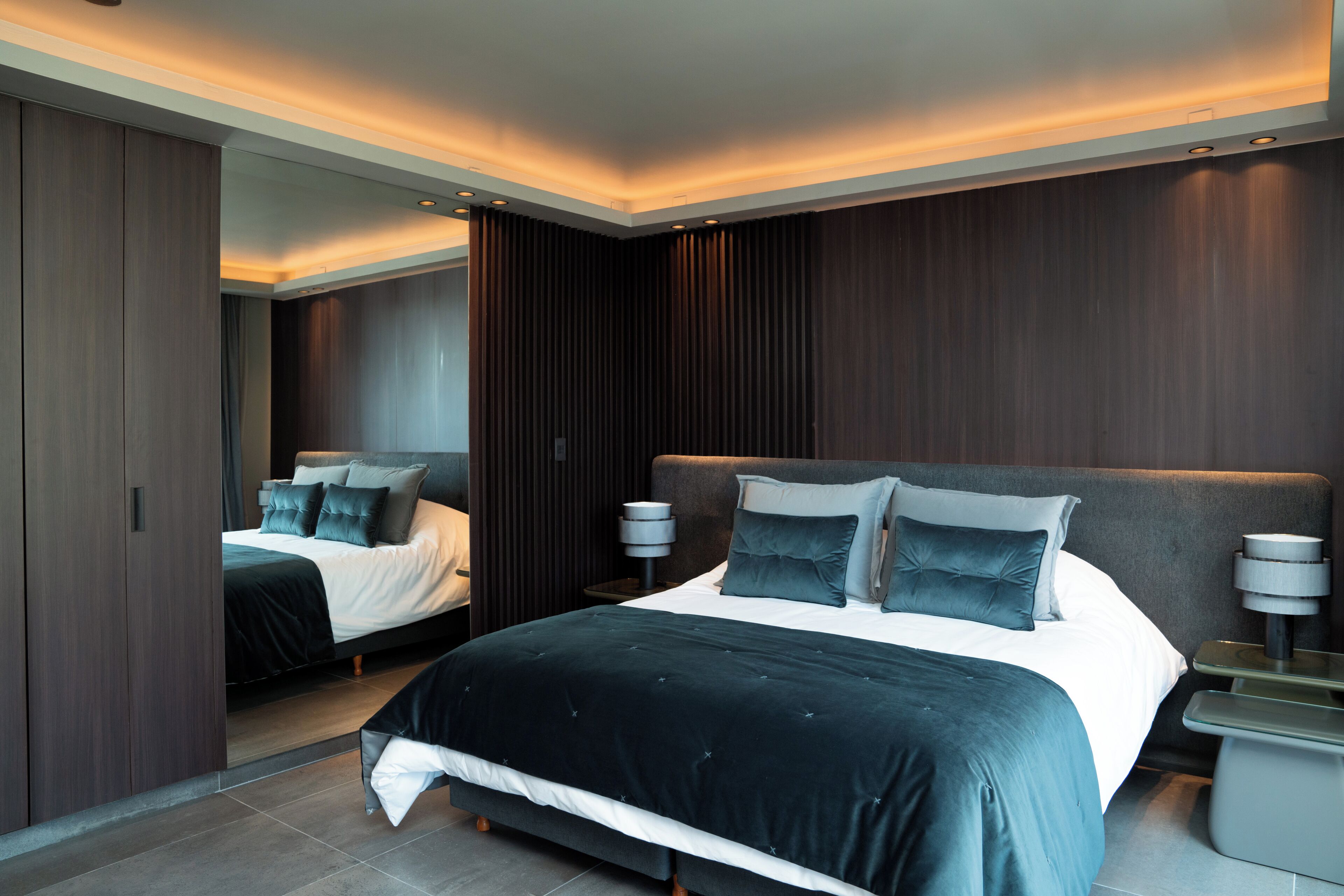 A modern bedroom with a large bed, a wardrobe, and a nightstand with a lamp.
