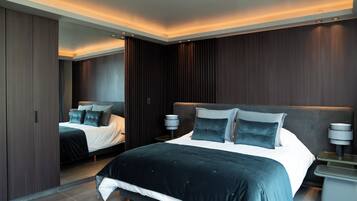 A modern bedroom with a large bed, a wardrobe, and a nightstand with a lamp.