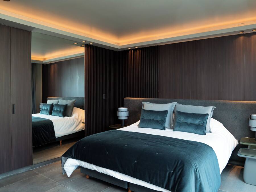 A modern bedroom with a large bed, a wardrobe, and a nightstand with a lamp.