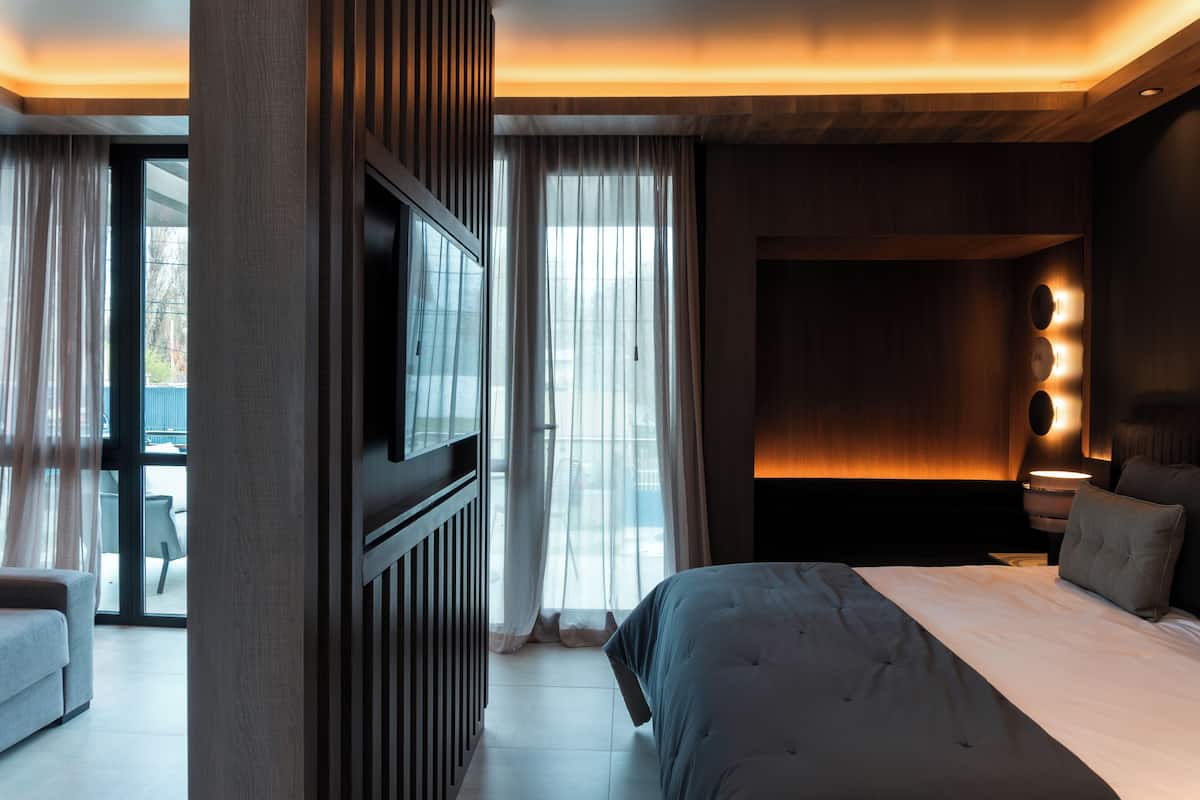 A modern hotel room with a large bed, a TV, and a view of the outdoors through the window.